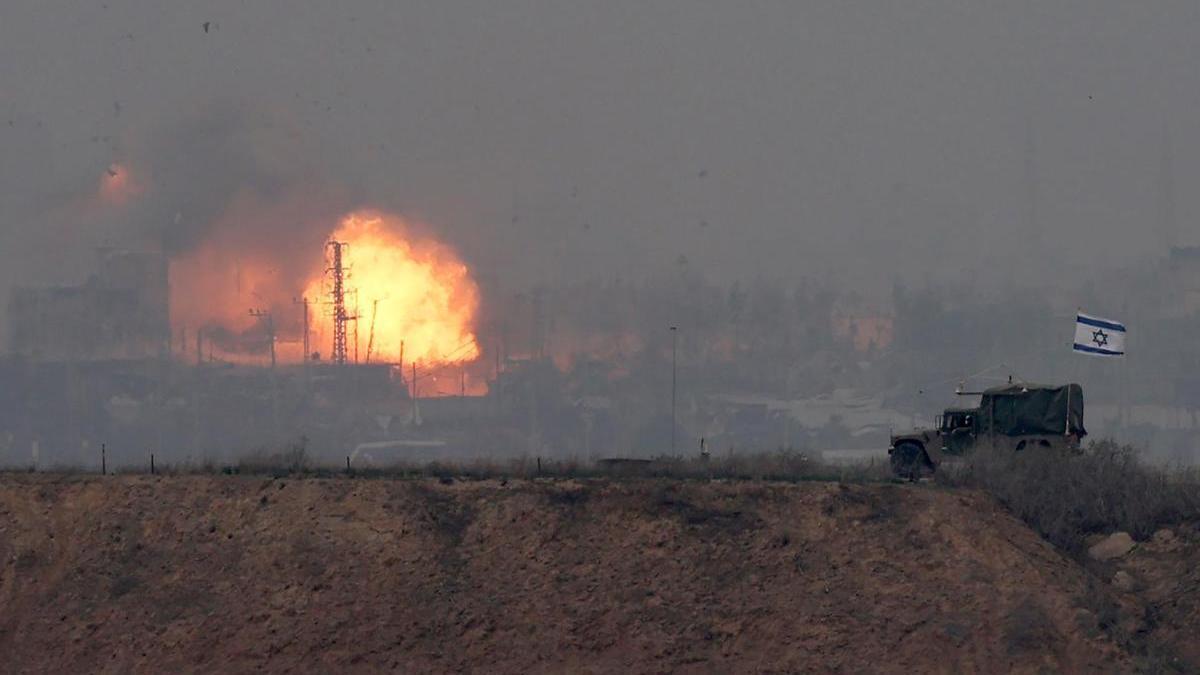 Un vehículo militar israelí avanza por la frontera con la Franja de Gaza en el sur de Israel mientras al fondo se produce una explosión.