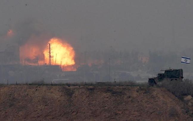 Un vehículo militar israelí avanza por la frontera con la Franja de Gaza en el sur de Israel mientras al fondo se produce una explosión.