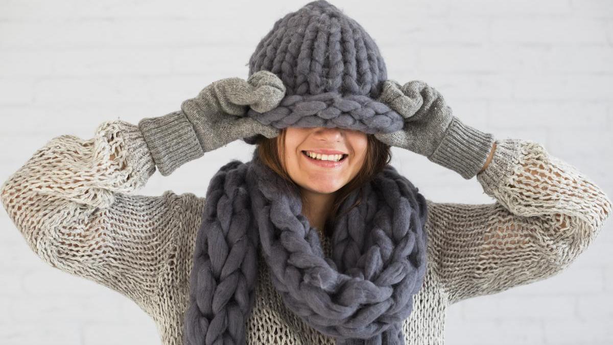 Chica joven sonriendo con guantes, gorro y bufanda para protegerse del frío en invierno