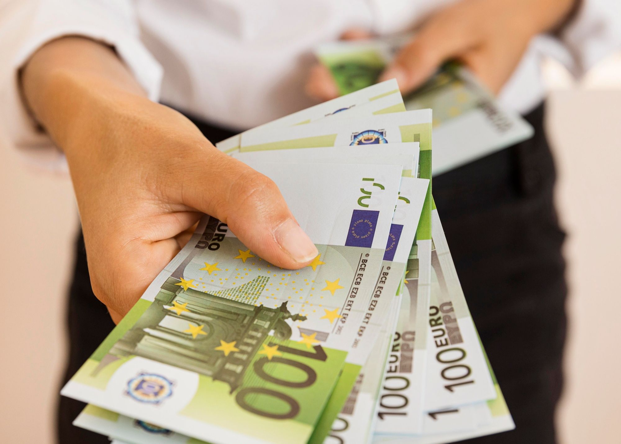 Un trabajador de banca entrega a un usuario billetes de 100 euros.