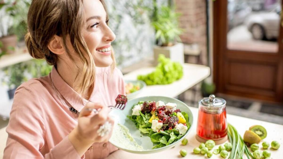 Chica sonriente come un plato con alimentos frescos y saludables.