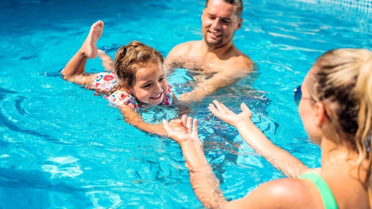 Padres juegan con su hija en la piscina y le enseñan a nadar.