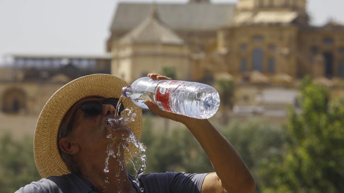 Un turista bebe agua con la Mezquita-Catedral de Córdoba al fondo.