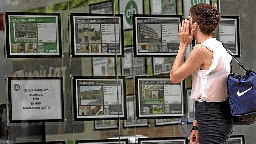 Una joven mira y compara precios de viviendas ante el escaparate de una inmobiliaria