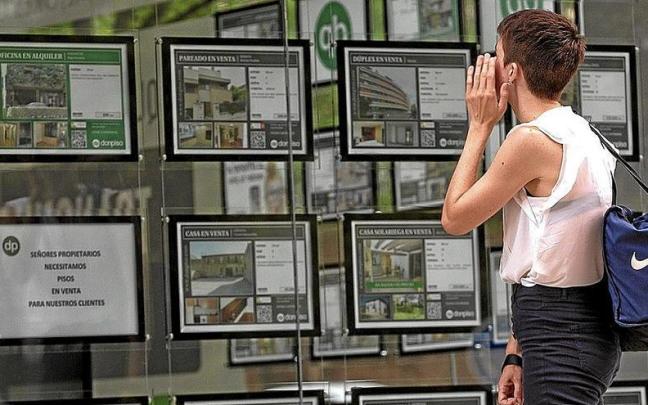Una joven mira y compara precios de viviendas ante el escaparate de una inmobiliaria