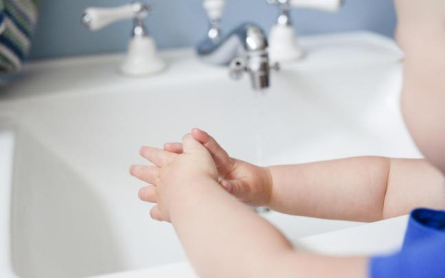 Imagen de un bebé con las manos mojadas frente a un lavabo