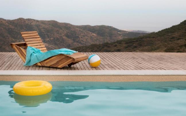 Tumbona de madera junto a la piscina y con vistas al monte.