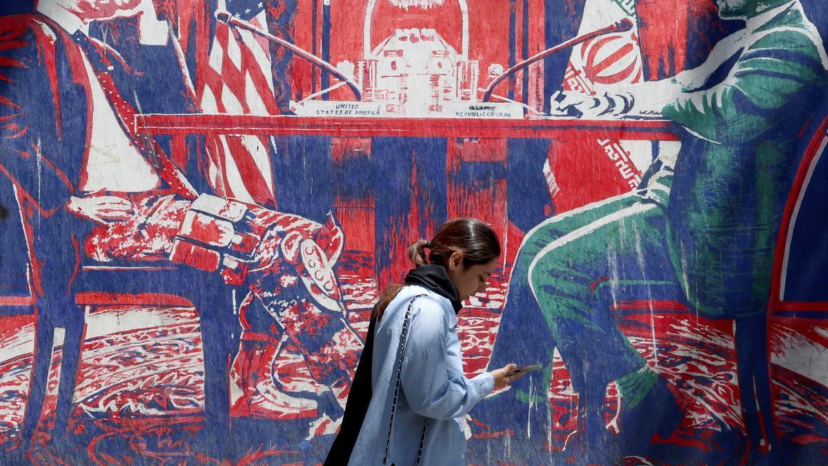 Una iraní camina junto a un mural antiamericano que representa las negociaciones entre Irán y EE.UU. en una mesa.
