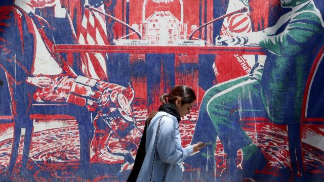 Una iraní camina junto a un mural antiamericano que representa las negociaciones entre Irán y EE.UU. en una mesa.