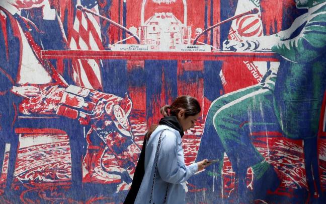 Una iraní camina junto a un mural antiamericano que representa las negociaciones entre Irán y EE.UU. en una mesa.
