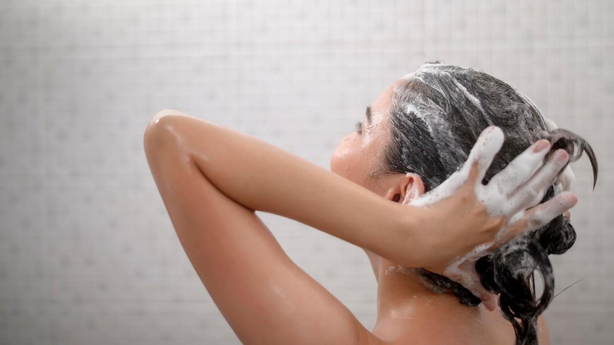 Una mujer se masajea el cabello en la ducha.