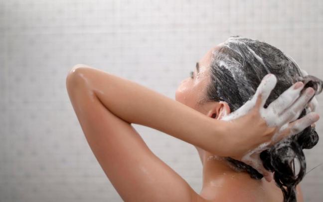 Una mujer se masajea el cabello en la ducha. Una mujer se masajea el cabello en la ducha.