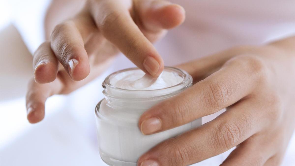 Primer plano de unas manos con un tarro de crema hidratante.