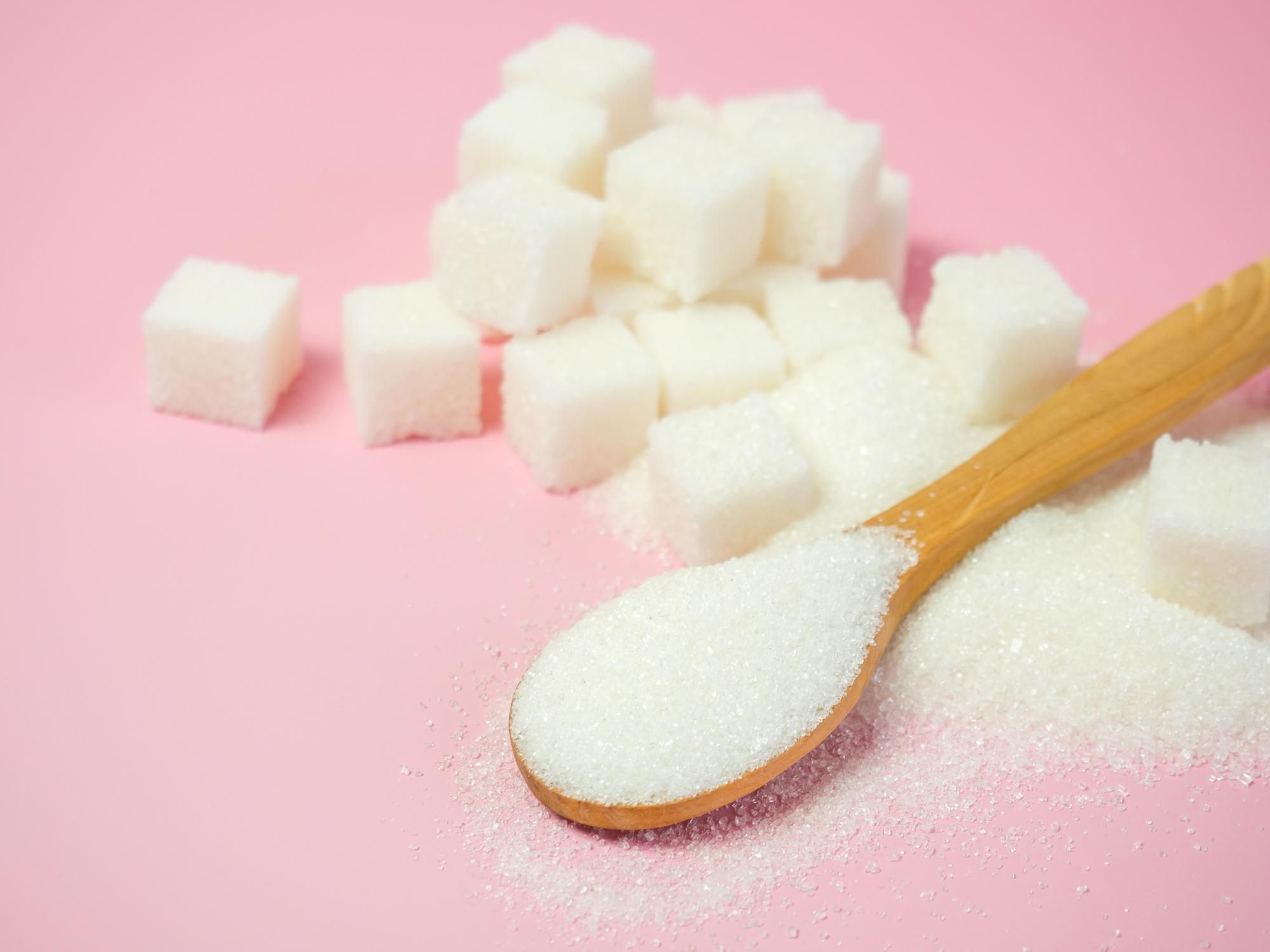 Azucarillos junto a una cuchara de madera llena de azúcar.
