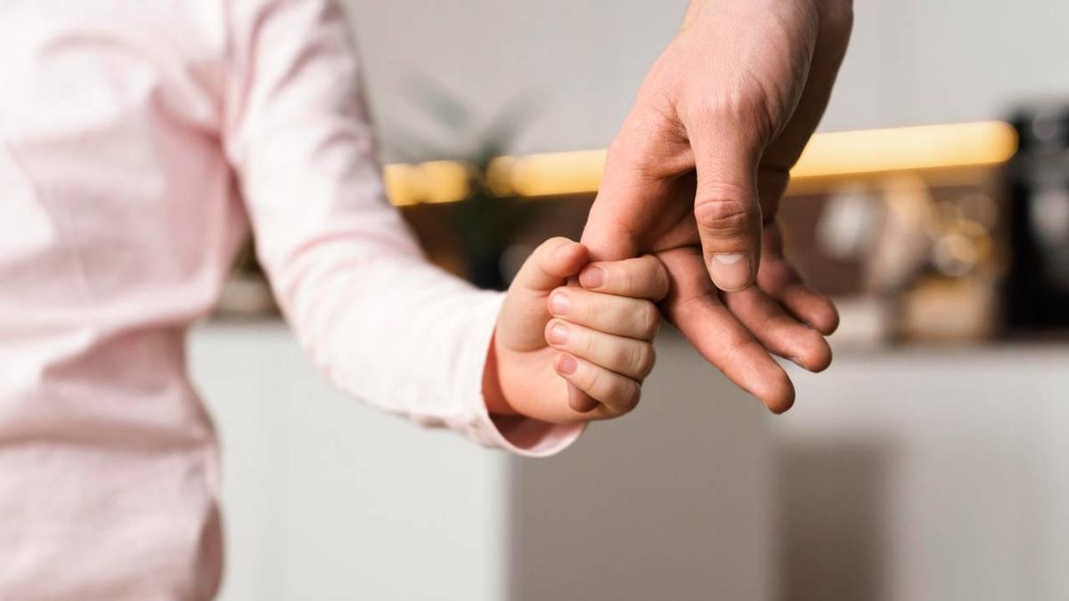 Un menor sostiene la mano de su progenitor