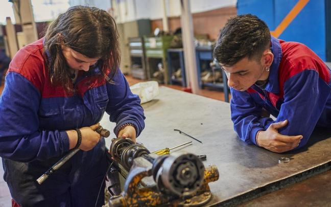 Una joven arregla un motor en un taller.