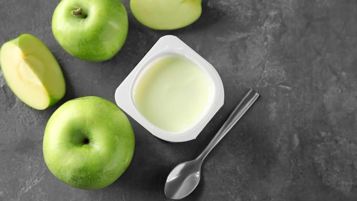Un vaso de yogur junto a varias manzanas.