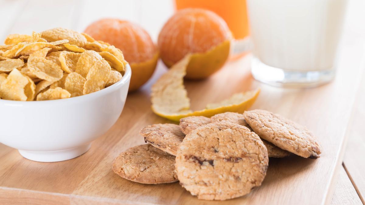 Mesa de desayuno con galletas, cereales, naranjas y un vaso de leche