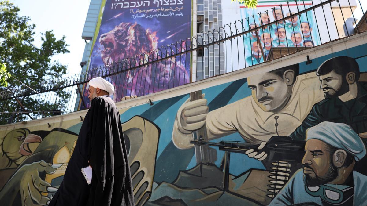 Un clérigo junto a una valla publicitaria contra Israel y EE.UU. en la que se lee en persa: “¿El rugido de un león o el chillido de un ratón?”.