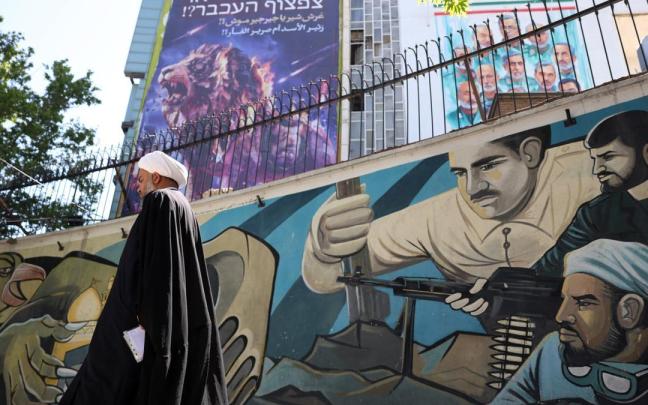 Un clérigo junto a una valla publicitaria contra Israel y EE.UU. en la que se lee en persa: “¿El rugido de un león o el chillido de un ratón?”.