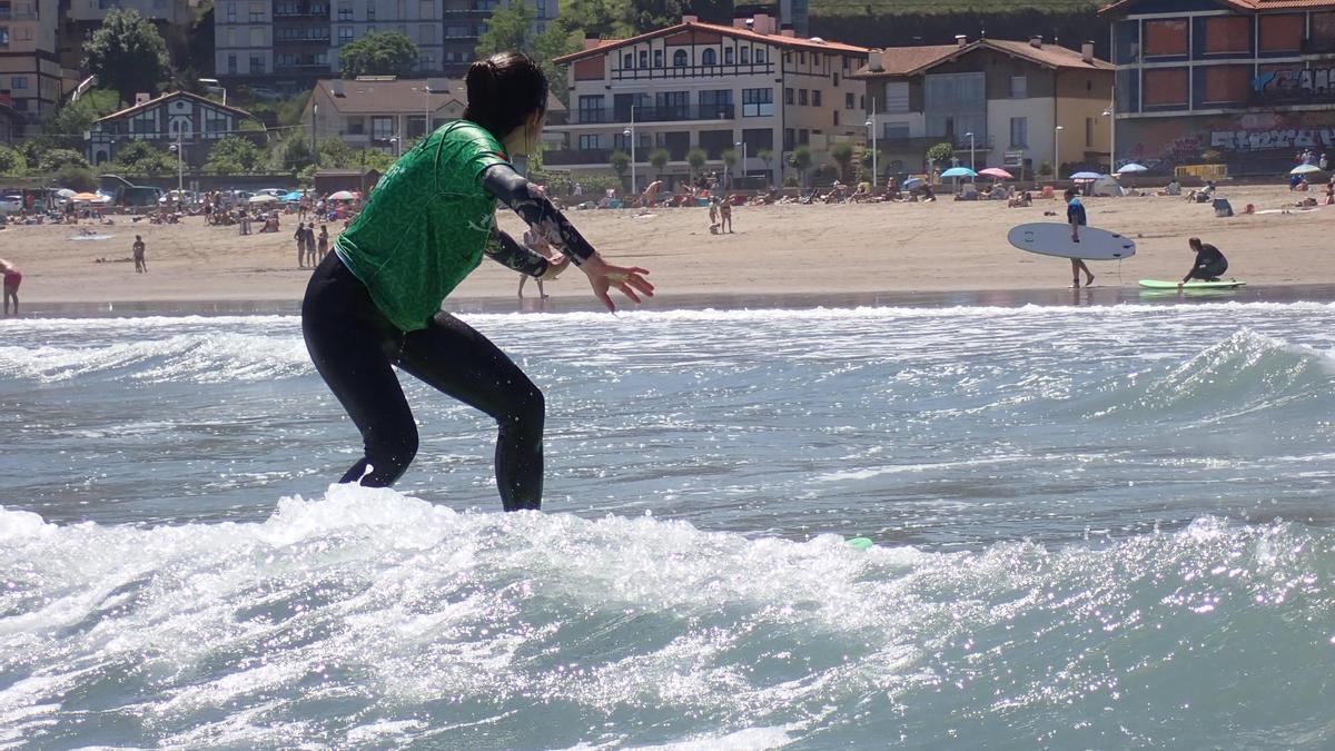 Una de las mujeres participantes en uno de los cursos llevados a cabo en Deba estos últimos años surfeando sobre una ola con la playa como fondo