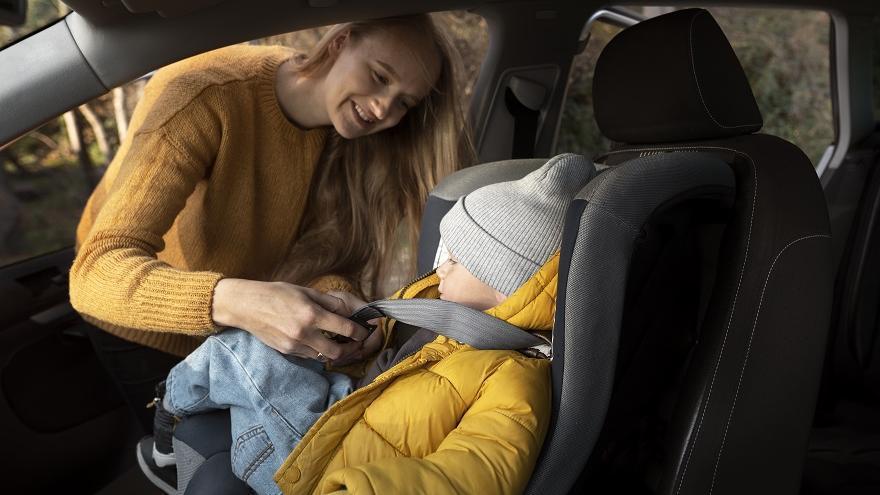 Una madre abrocha el cinturón de una sillita de coche infantil.