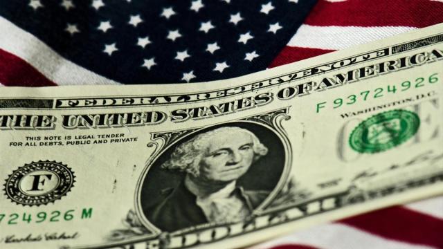 Un billete de un dólar sobre una bandera de Estados Unidos. Un billete de un dólar sobre una bandera de Estados Unidos.