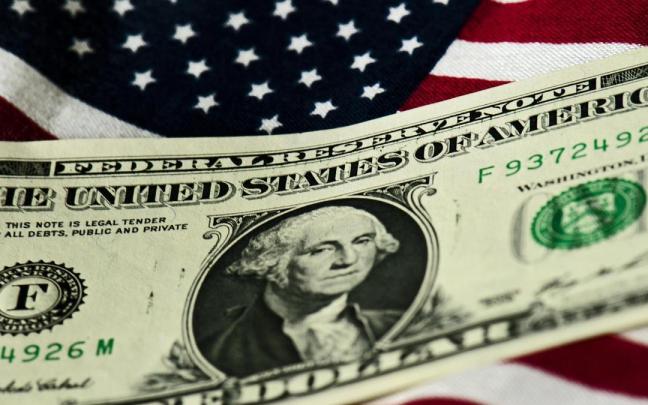 Un billete de un dólar sobre una bandera de Estados Unidos. Un billete de un dólar sobre una bandera de Estados Unidos.