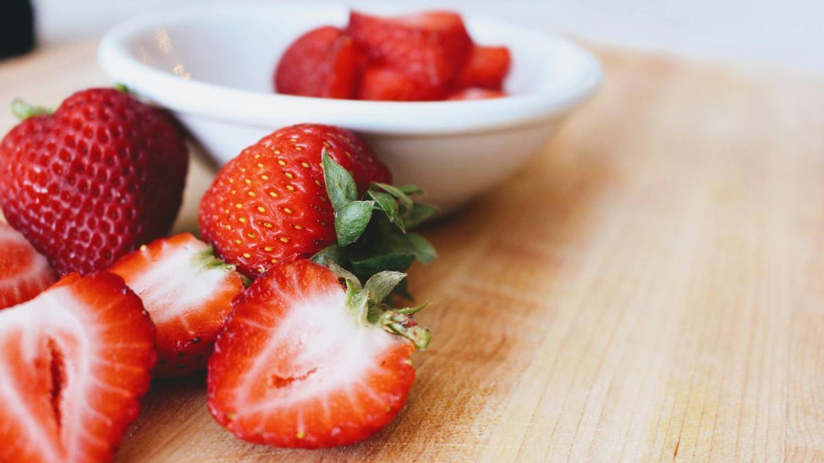 Fresas cortadas por la mitad al lado de un bol de color blanco.