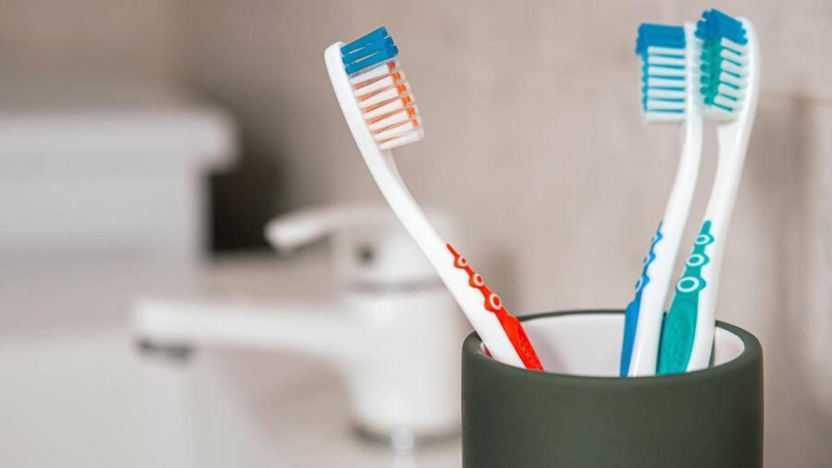 Tres cepillos de dientes juntos en un vaso al lado del grifo del baño