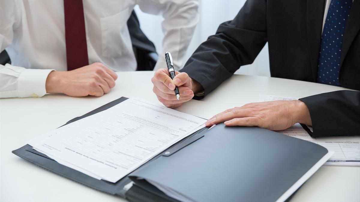 Dos hombres trajeados firmando un documento.