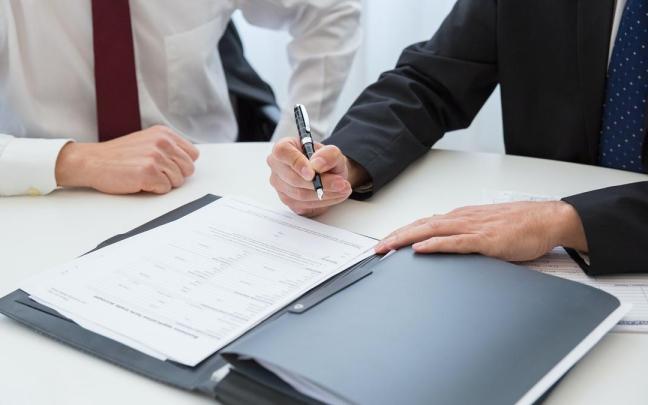 Dos hombres trajeados firmando un documento. Dos hombres trajeados firmando un documento.