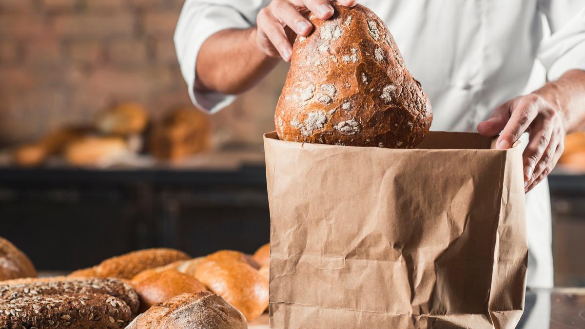 Un panadero guarda una hogaza de pan en una bolsa de papel.