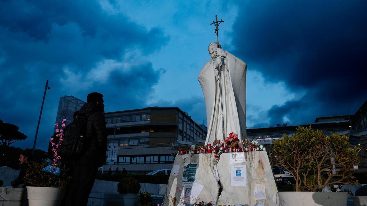 Un hombre observa la estatua de Juan Pablo II a las puertas del Hospital Gemelli.
