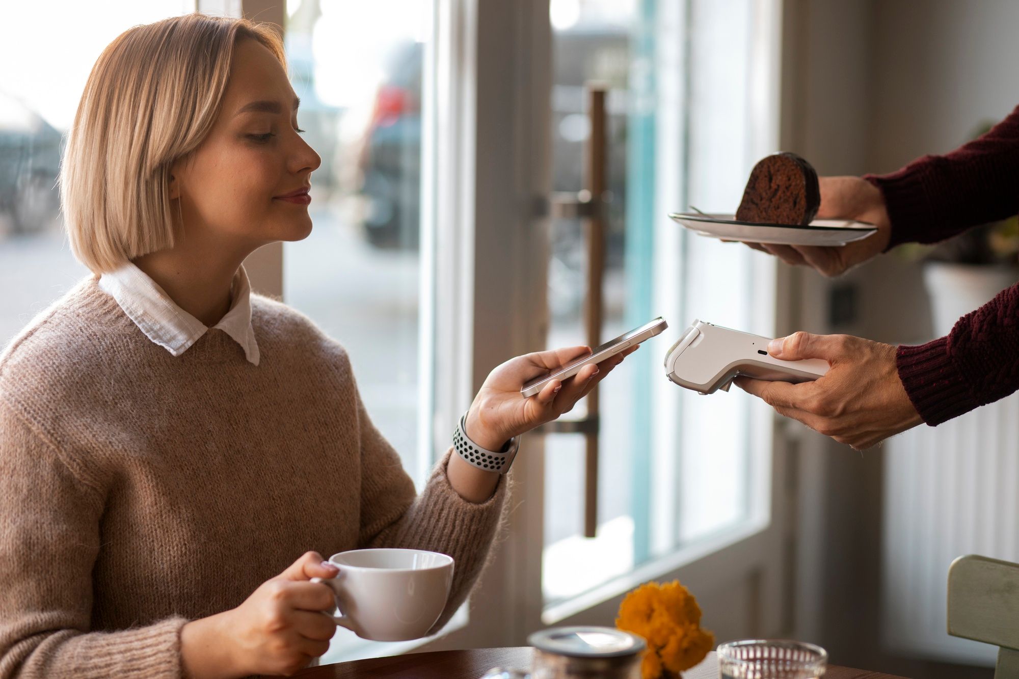 Una mujer acerca el móvil al datáfono para pagar el desayuno en una cafetería.
