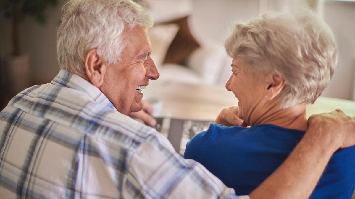 Una pareja de personas mayores sonríen mientras se miran.