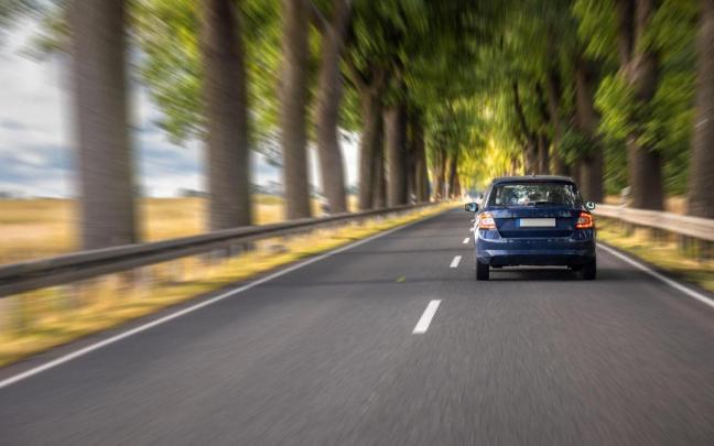 Un coche circula a gran velocidad por una carretera arbolada.