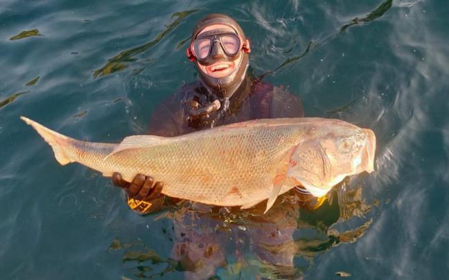 Haritz Ayarza, en el agua, enseñando la lubina que ha capturado.