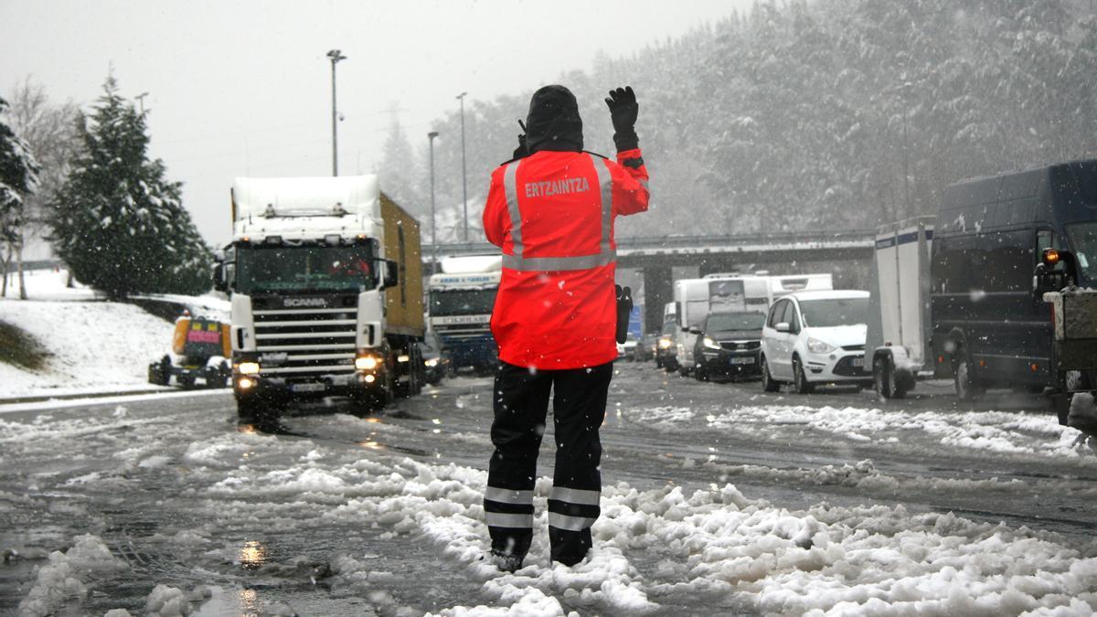 Un ertzaina dirige el tráfico en una carretera nevada.