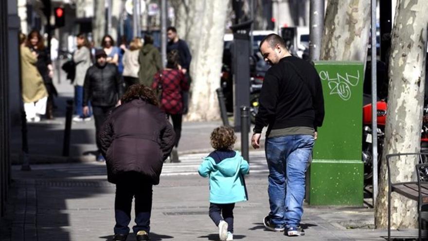 Unos padres pasean junto a su hija por la calle.