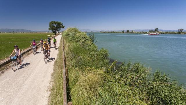 Un grupo de ciclistas recorre el Camí de Sirga mientras un barco turístico surca el Ebro.