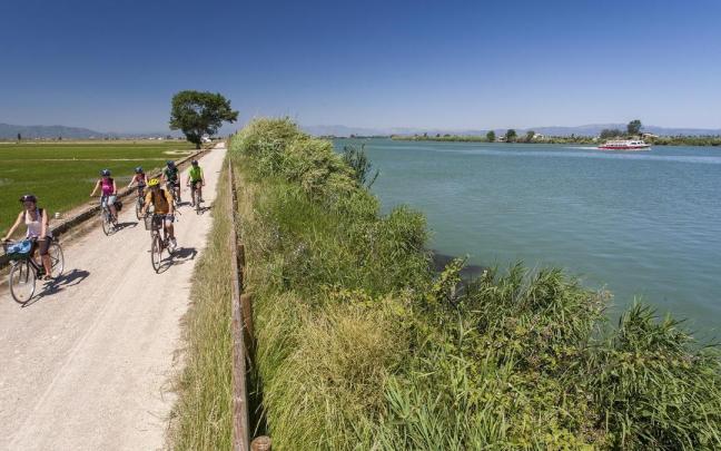 Un grupo de ciclistas recorre el Camí de Sirga mientras un barco turístico surca el Ebro.