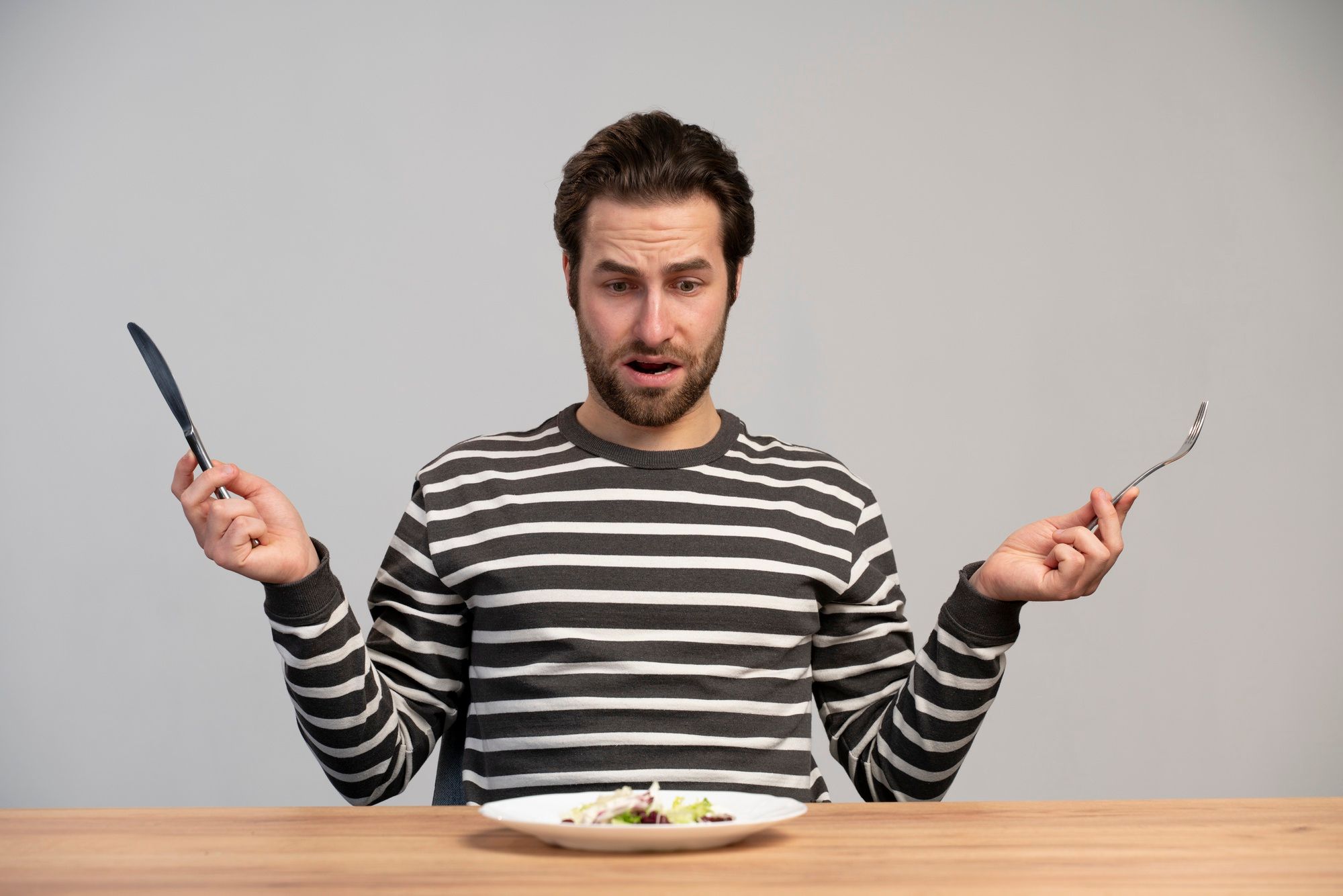 Un hombre delante de un plato con una pequeña ración de ensalada.