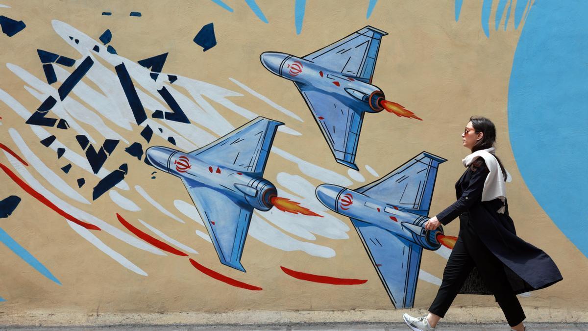 Iraní camina junto a un mural contra EE.UU. e Israel en una calle de Teherán.