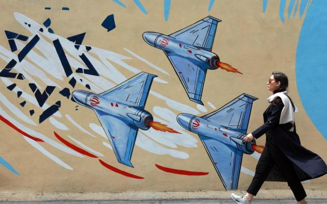 Iraní camina junto a un mural contra EE.UU. e Israel en una calle de Teherán.