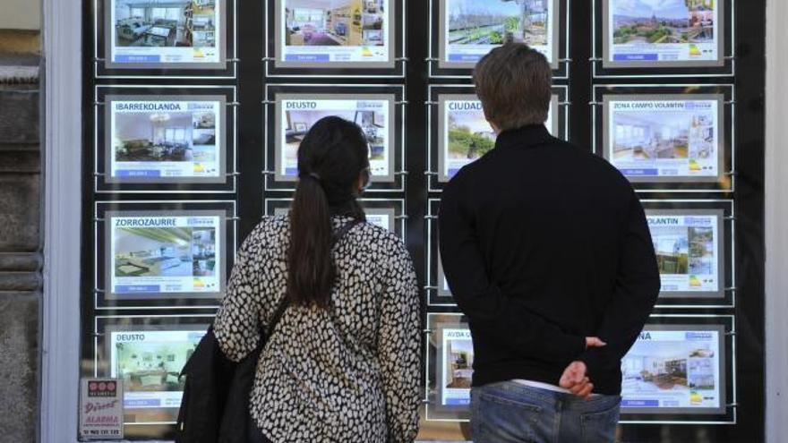 Dos jóvenes observan el escaparate de una inmobiliaria.
