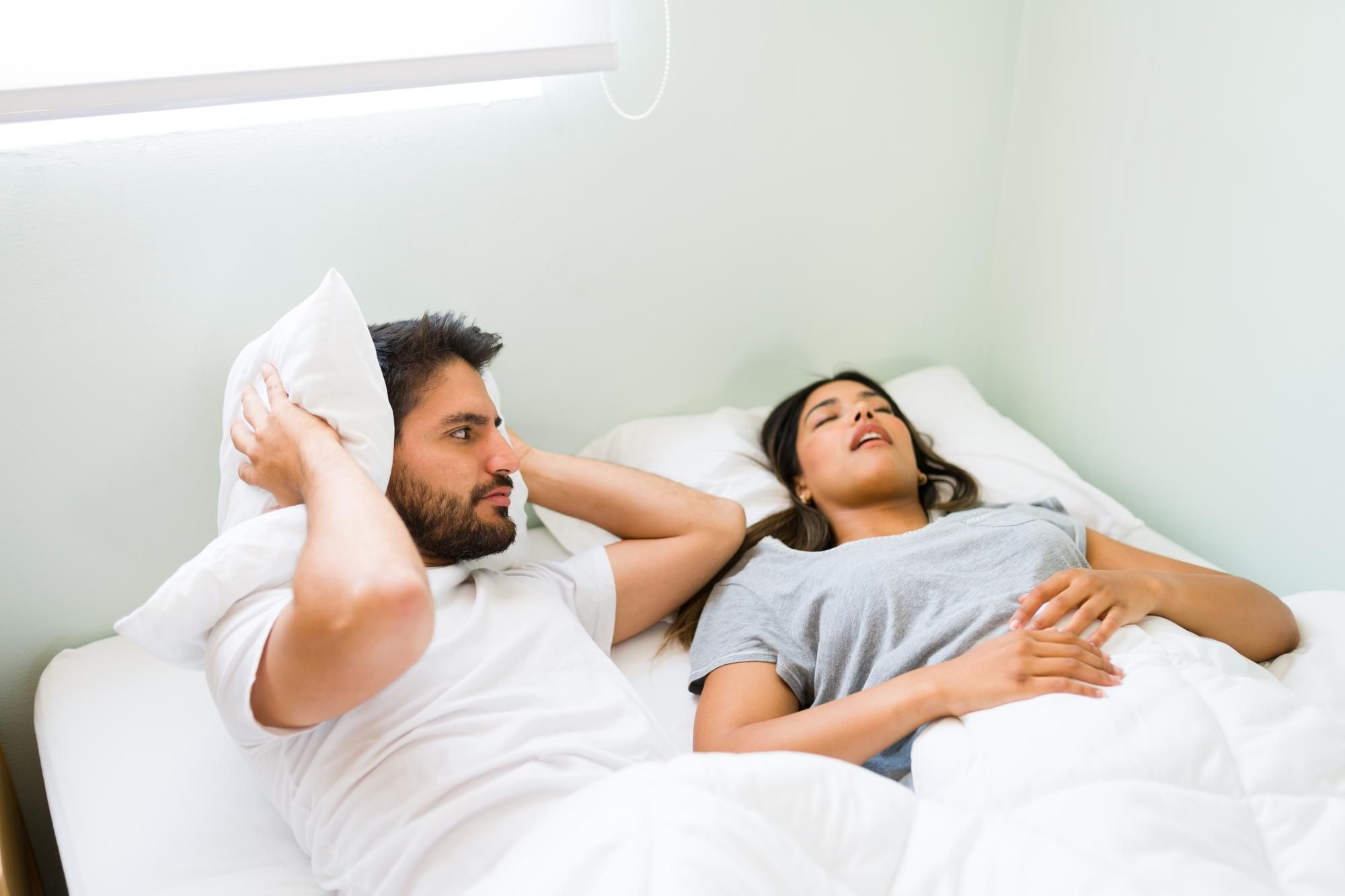 Un hombre se tapa los oídos con la almohada mientras su pareja ronca.