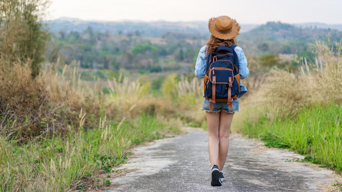 Una mujer camina por un sendero cargando una mochila a su espalda.