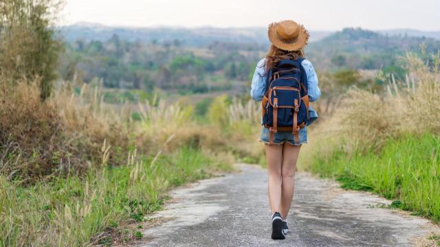 Una mujer camina por un sendero cargando una mochila a su espalda.