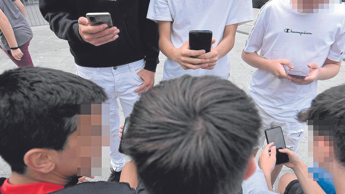 Un grupo de menores, ajenos a esta información, consultan sus teléfonos móviles reunidos en una calle de Bilbao.